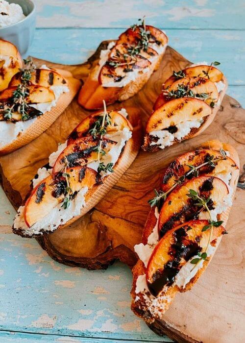 peach and ricotta crostini on a wooden board, more ricotta on the background