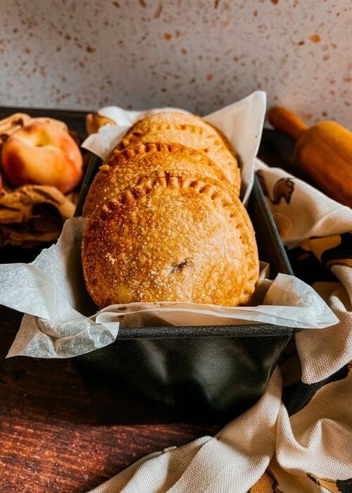peach hand pies in a tin, peaches on the left and a rolling pin on the right