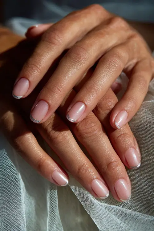 Bridal fingers resting gently on veil fabric, short ballerina nails in pale pink with diagonal silver chrome tips, soft dreamy lighting
