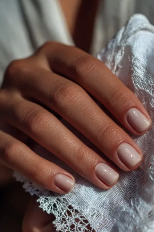 Bride’s hand holding a lace handkerchief, short square nails in sheer white with subtle shimmer and micro pearl studs, romantic vintage background 