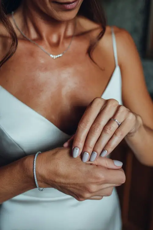 Soft shot of bride’s hands adjusting bracelet, short square nails in light gray with a matte finish and a silver half-moon detail at the base