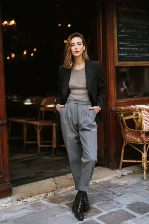 A woman in straight-leg trousers paired with a fine knit top, structured wool blazer, and polished leather ankle boots, standing outside a traditional café during winter