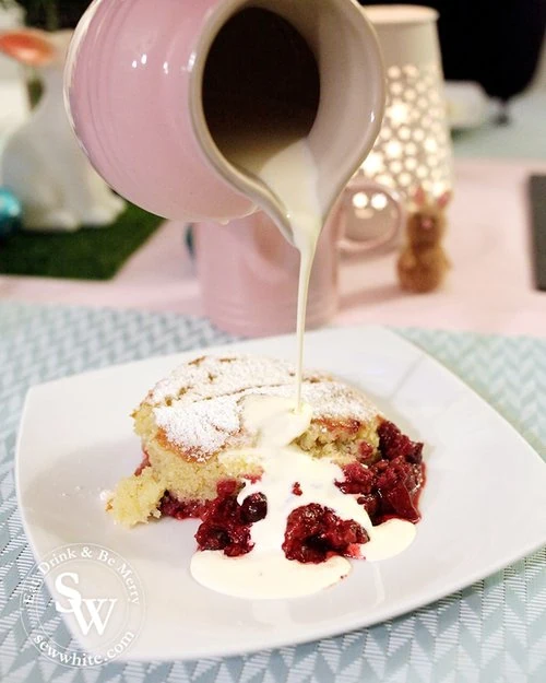 Pouring cream over the summer fruit sponge pudding. The rich red berries and golden sponge glisten on the plate.