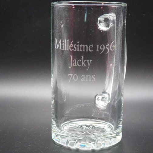Chope à bière en verre transparente gravée avec l'inscription "Millésime 1956 Jacky 70 ans" sur fond noir.