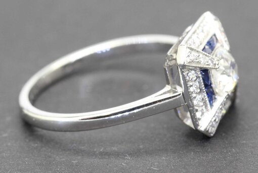 Engagement ring with a central diamond and blue sapphires, set in a silver band.