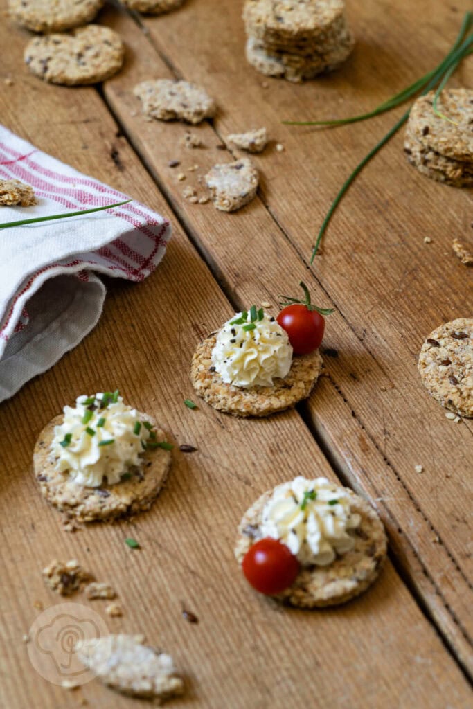 Schnelle Cracker 2 Cracker auf einem Brett. Teilweise mit einer Frischkäsecreme und Tomaten.