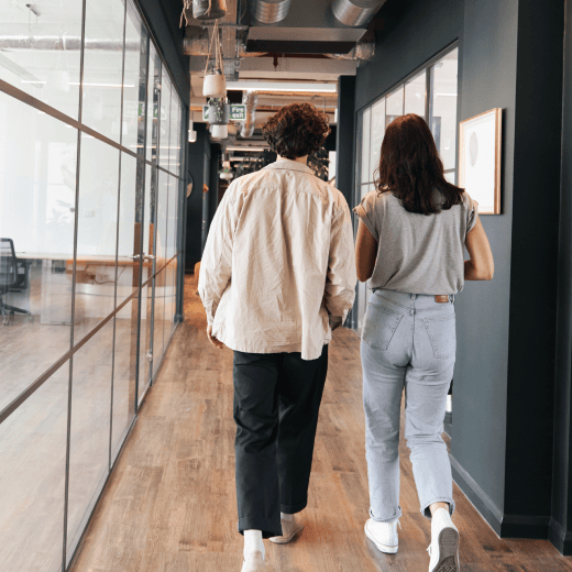Two co-workers walking towards their desk in the office.