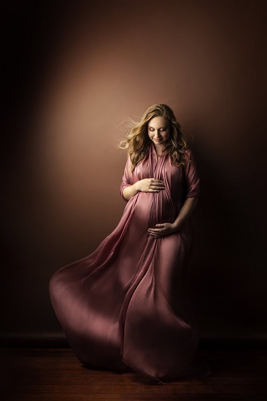 En gravid kvinne i vakker rosa gravidfotografering, bærer flytende kjole, spår en snart fødsel, inspirerende og kunstnerisk gravidfoto.
