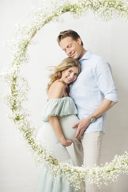 Lekre gravidfotobilder av lykkelige gravide med partner i en myk, romantisk fotosetting med blomsterkrans. Perfekt for gravidtoget og å fange det nevnte øyeblikket.