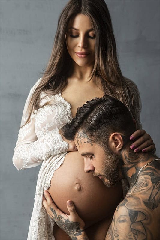 Moden gravid kvinne med mann som kysser hennes stolte gravidmage, intim gravidfotografering, vakkert og meningsfullt gravidbilde.