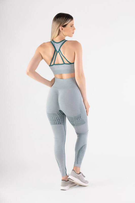 mujer de espaldas con su mano en la cintura luce sujetador y short deportivo color azul verdoso claro