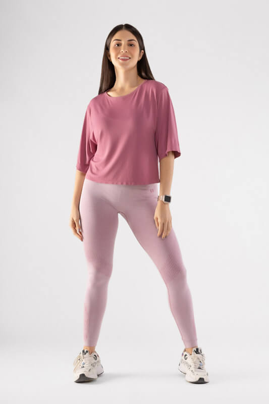 mujer de frente con sus brazos hacia abajo y cabello suelto luce crop top de color rosado oscuro y leggins deportivo color rosado