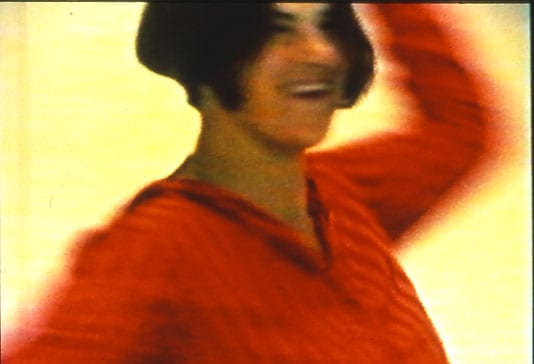 A grainy video still from the film Why I Never Became a Dancer by Tracey Emin, showing the artist dancing in a vibrant red top against a yellow-toned background.