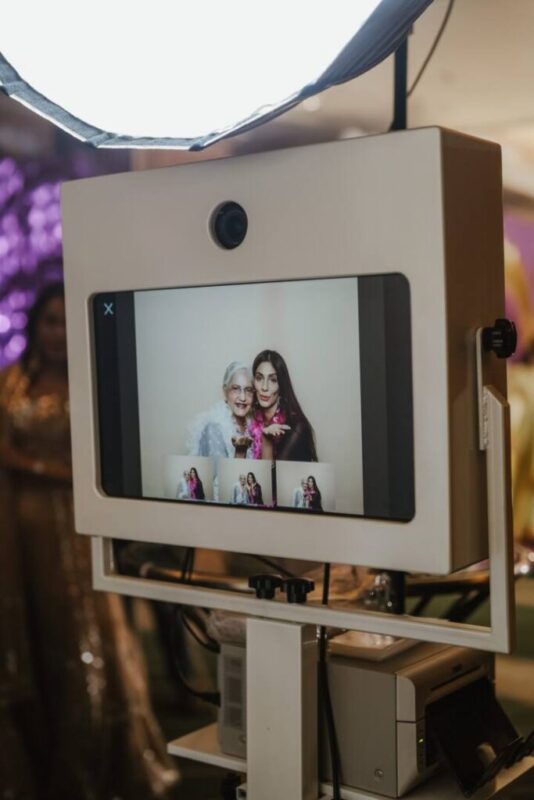 Studio photo booth screen showing a live preview of two guests, lit by a large softbox