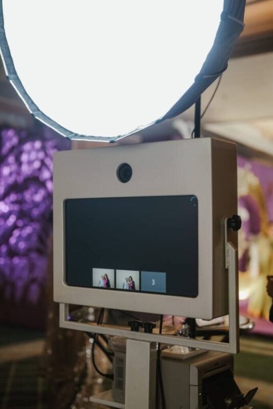 White studio photo booth camera kiosk with preview screen under a large round softbox light