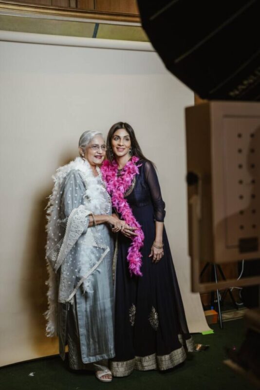 Two women in Indian outfits with feather boas posing at the white studio booth backdrop