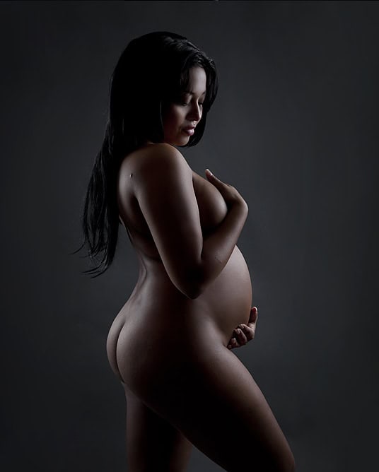 Elegant gravidfotografi av gravid kvinne med lang svart hår, som beskytter sitt prenatalpreg gjennom kunstneriske lys- og skyggeeffekter. Perfekt for gravidfoto, graviditet, forlovedesr og spesielle øyeblikk.
