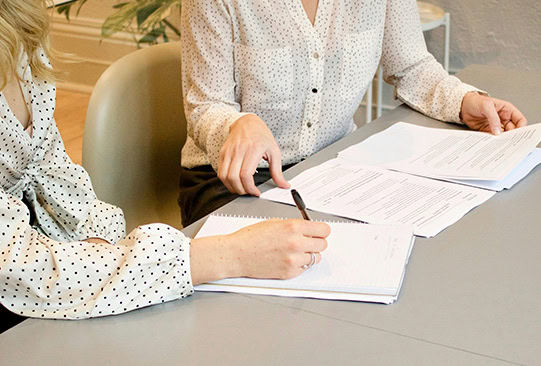 The women are sitting at the table with documents in their hands.