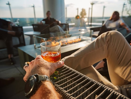 A man dressed in business casual enjoys a cocktail on the patio of 1000 Social, a modern office building that includes retail, dining, and social spaces.