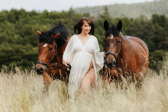 Frau mit Babybauch und ihren beiden Pferden auf einer Wiese