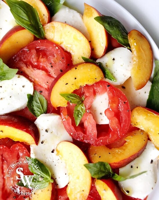 A colour dish of peach slices, mozzarella, tomatoes, basil and black pepper.