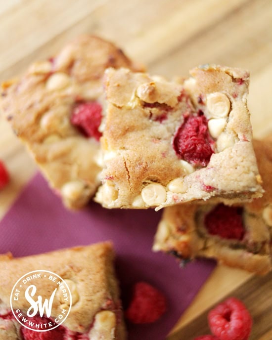 golden baked raspberry white chocolate cookie traybake on a purple napkin and wooden bench.