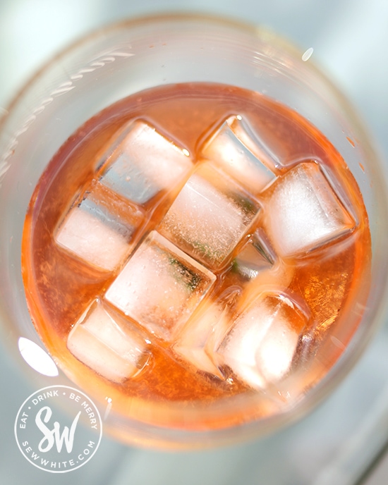 Golden orange Aperol cocktail with apple juice and bright white ice cubes ready to be topped up with cloudy apple juice