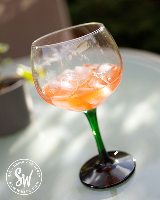 Bright orange Aperol Apple Cocktail in a large cocktail bowl glass. 