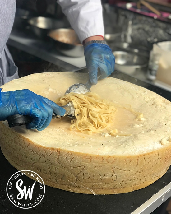 cooked pasta being rolled in a wheel of cheese at the love wimbledon market.