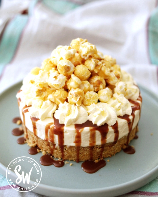 toffee drizzle on a cheesecake studded with toffee pieces and toffee sauce drizzling over. On top toffee popcorn overflows.