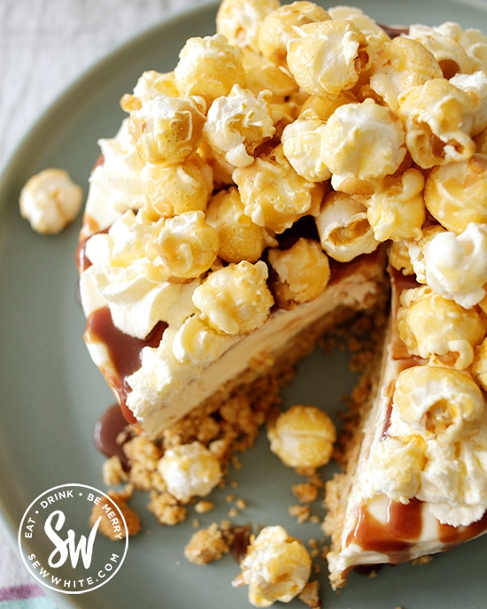 cheesecake with toffee sauce drizzled over and popcorn on top on a blue plate.