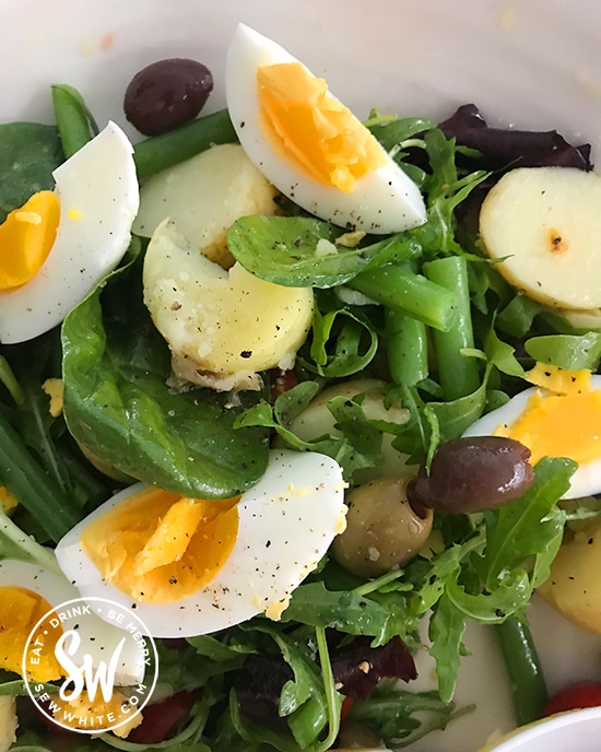 sliced boiled egg pieces sprinkled with pepper, with green beans and new potatoes on a bed of salad leaves in the easy egg salad