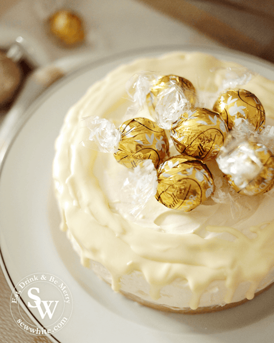 Baileys and White Chocolate Cheesecake topped with golden lindt truffles and with a white chocolate drip.