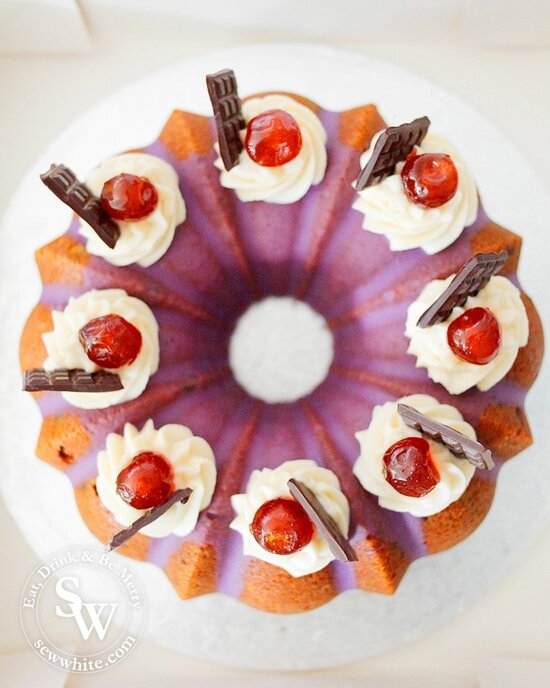 A beautiful easy black forest bundt cake topped with buttercream swirls and mini chocolate bars and glace cherries