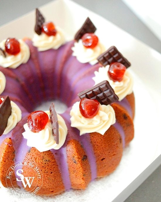 the cutest Black Forest cake in a bundt tin and decorated with purple glaze, butter cream blobs and topped with a glace cherry and mini chocolate bar.