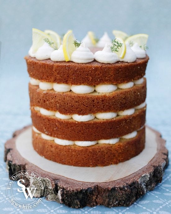 A golden baked four layer gin cocktail cake with blobs of buttercream in between each layer and decorated with lemon slices and fresh thyme on top.