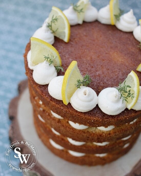 Top view of the gin layer cake which is a beautiful golden brown gin layer cake topped with white buttercream blobs along with fresh lemon slices and fresh thyme.
