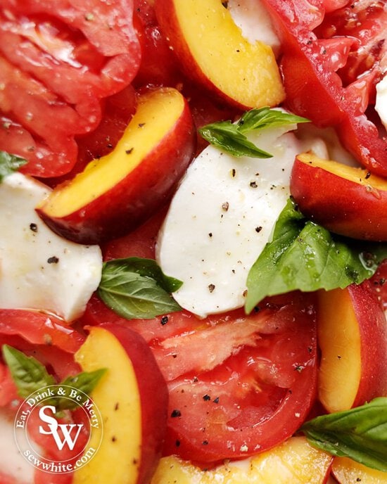 A close up of Heirloom Tomato and Peach Salad with large slices of mozzarella, cracked black pepper and fresh basil. Drizzled with olive oil.