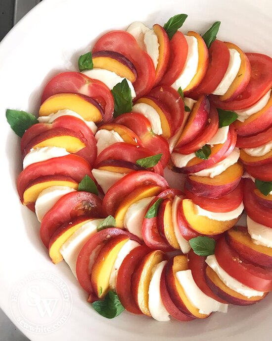 Tomato Peach Salad laid out in a circle for presentation stacked together studded with basil leaves. 