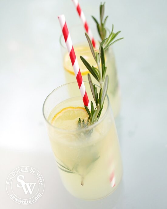 Bright red and white paper straws in fresh rosemary lemonade with a green sprig of rosemary.