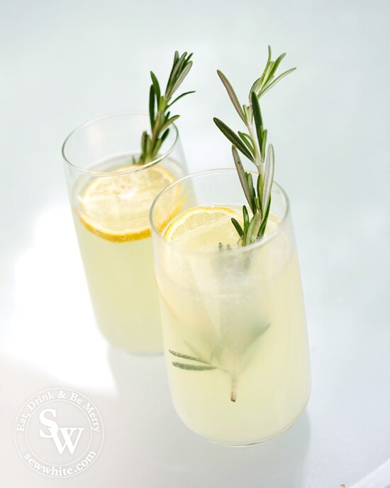 Elderflower and Rosemary Lemonade in tall glasses  with large slices of lemon and a bright green sprig of rosemary.