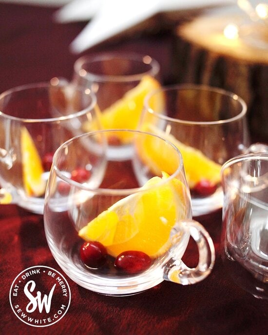 Glass punch glasses with a slice of orange and fresh cranberries in for a Christmas cocktail.