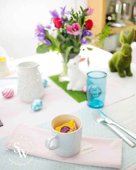 pastel Easter table with pink napkins and settings of cups with mini eggs. 