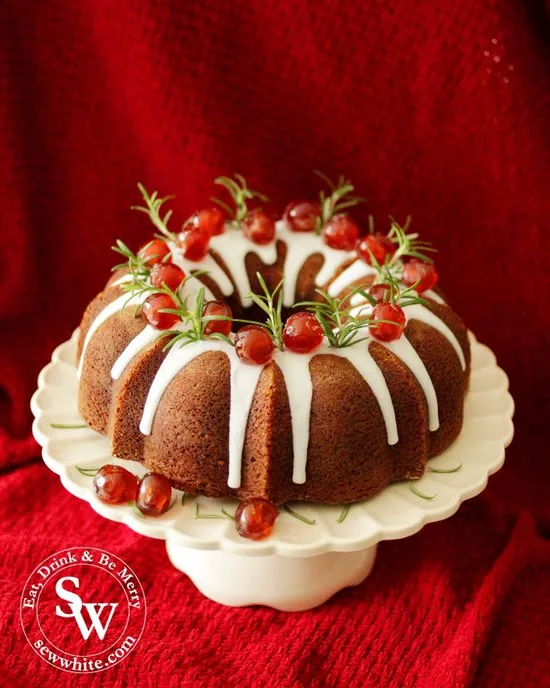 Black Forest Christmas Bundt Cake on a white cake stand decorated with rosemary and red galce cherries.