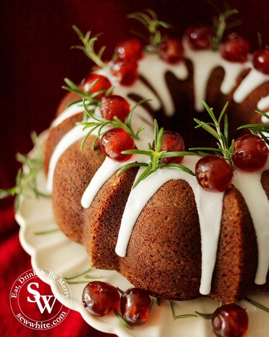 close up of a christmas bundt cake with white icing drizzle down decorated with rosemary sprigs and cherries