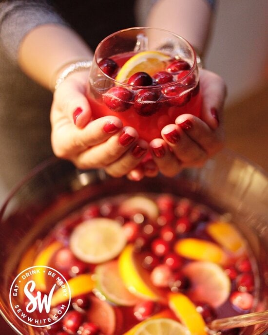 Two hands holding a Christmas Cranberry Punch glass cup with fresh cranberries and orange slice in.