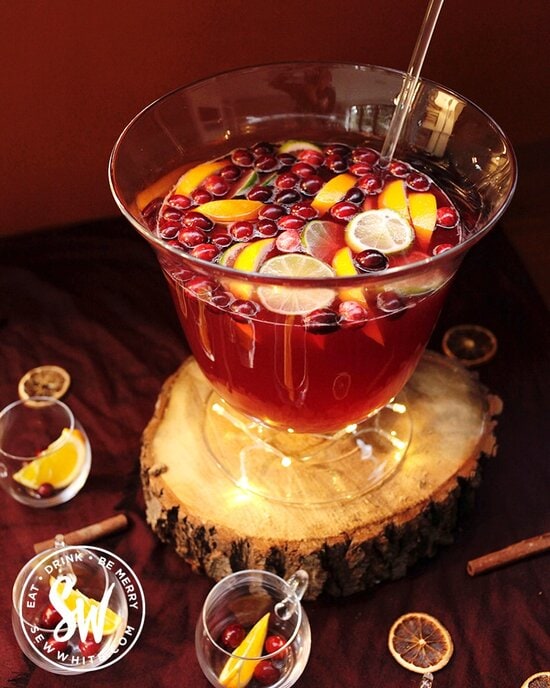 Red Christmas Punch with fresh cranberries and orange slices in for decorations on a red table.