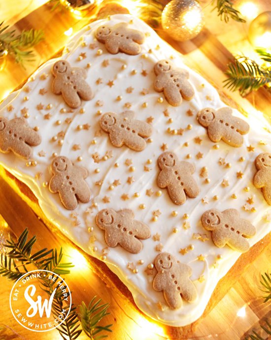 Gingerbread traybake decorated with cream cheese frosting and decorated with gingerbread men biscuits on a wooden board