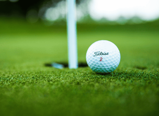 Golf ball close-up on the putting green with a flagstick in the background.