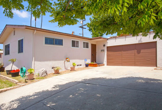 Mid-century ranch style home at 3727 Suffolk Drive in Rolando Park with a wide concrete driveway, brown garage door, and low-maintenance front landscaping under a leafy tree.